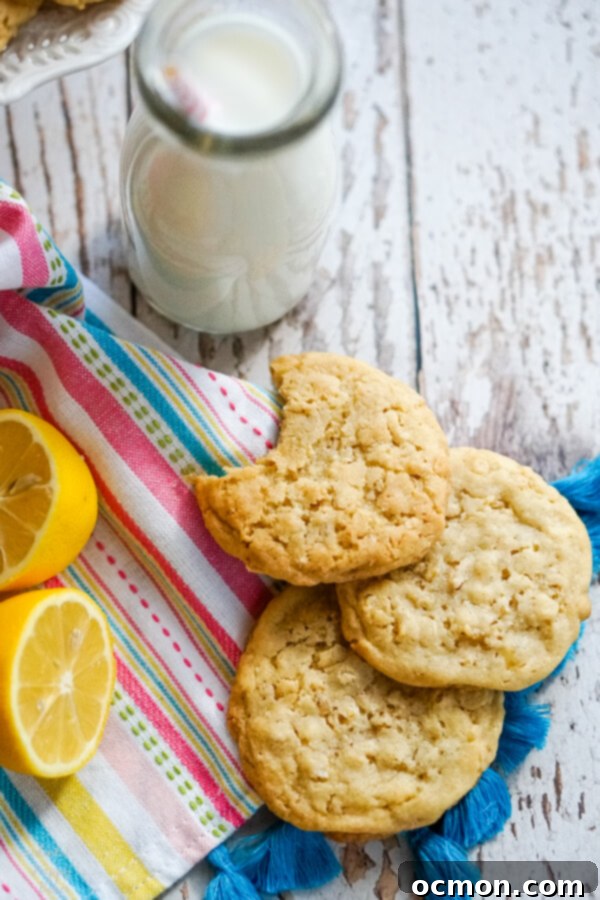 Zesty Lemon Cowboy Cookies 7 A stack of golden Lemon Cowboy Cookies rests on a striped towel, perfectly paired with a refreshing bottle of milk, embodying a delightful snack.