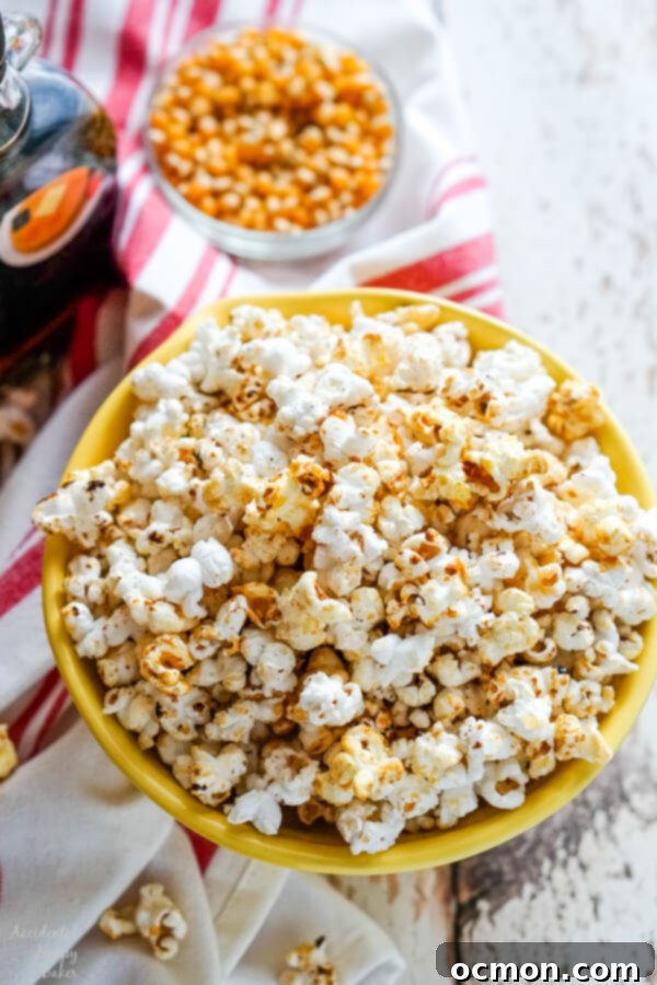 A bowl of kettle corn with some unpopped kernels and maple syrup in the background. 