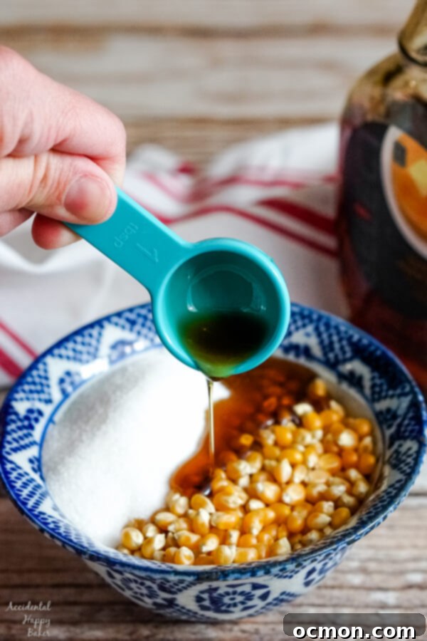 Maple syrup is added to a bowl of popcorn kernels and sugar. 