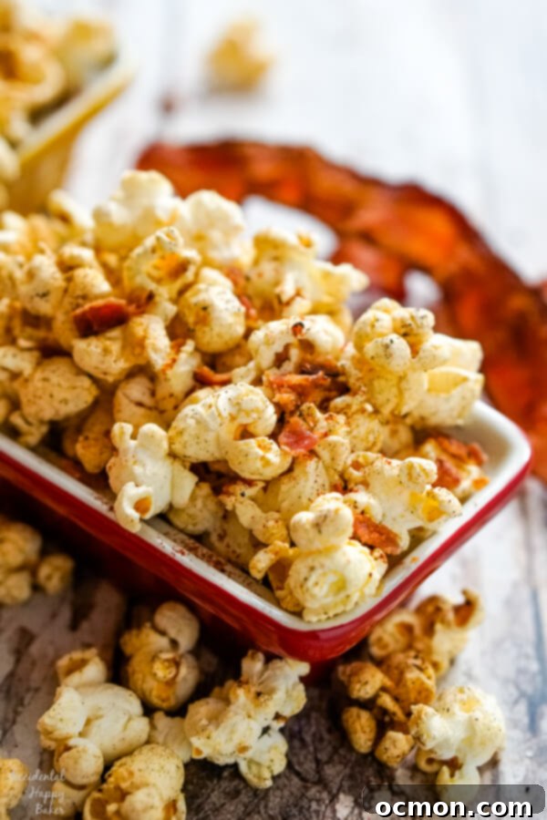 A red bowl full of popcorn with a piece of bacon in the background.
