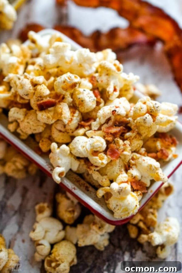 A close up image of a bowl of popcorn with bacon pieces and other seasonings. 