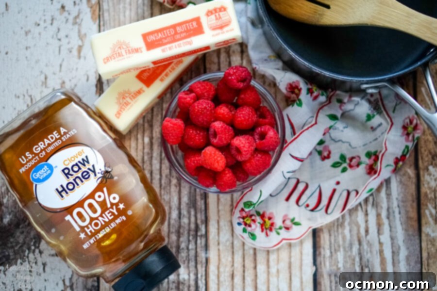 Whipped Raspberry Honey Butter 4 A simple arrangement of three key ingredients: a jar of golden honey, a block of unsalted butter, and a bowl of fresh, ripe raspberries, next to a small saucepan.