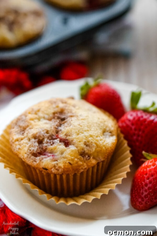 Sweet and Tangy Strawberry Rhubarb Muffins 3 A strawberry rhubarb muffin on a plate with 3 fresh strawberries, highlighting its deliciousness.