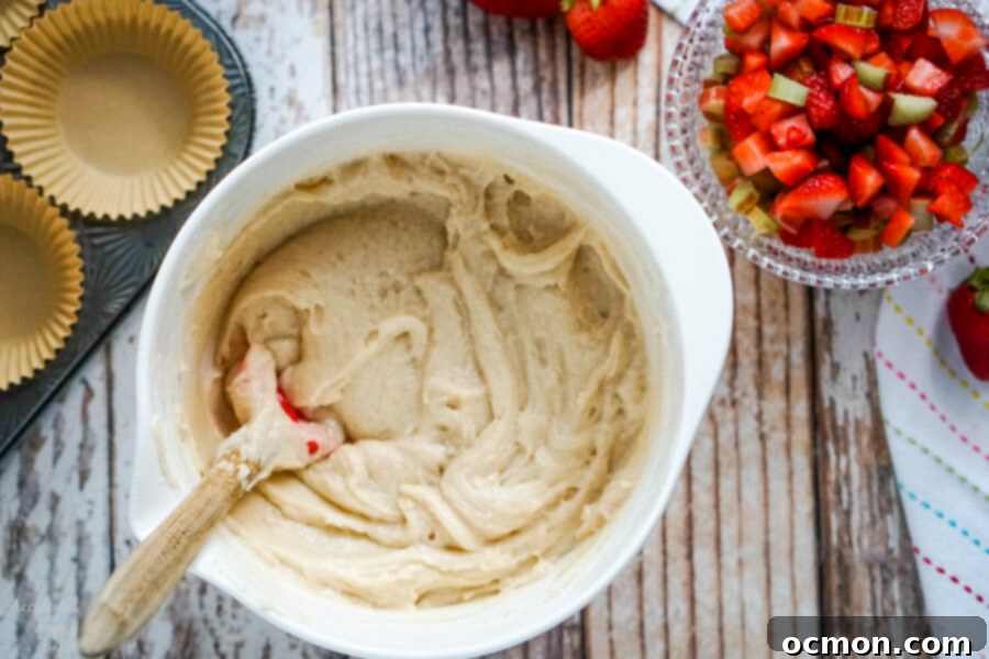 Sweet and Tangy Strawberry Rhubarb Muffins 4 A white batter bowl full of muffin batter next to a bowl of chopped strawberries and rhubarb, ready for mixing.