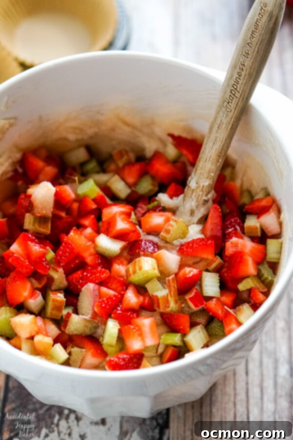 Sweet and Tangy Strawberry Rhubarb Muffins 5 Folding in the chopped strawberries and rhubarb into the muffin batter, showcasing the vibrant ingredients.
