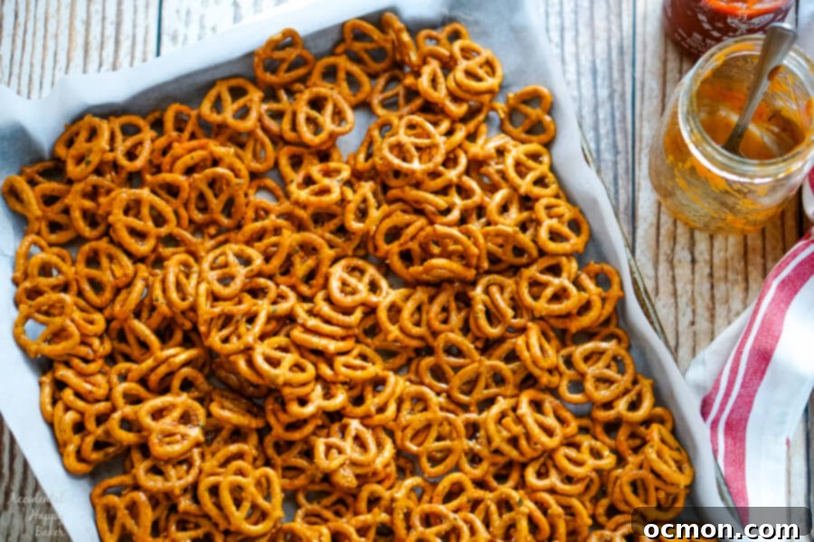 Spicy sriracha ranch pretzels spread out in a single, even layer on a parchment-lined baking tray, ready to be baked to a crispy finish.