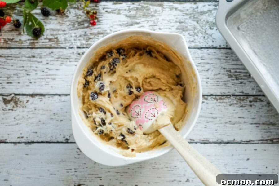 Blackberry Bliss Loaf 3 A close-up shot of blackberry bread batter in a mixing bowl after the berries have been gently folded in, showing vibrant purple streaks.
