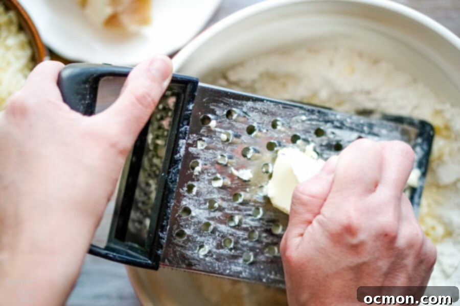 Frozen unsalted butter being grated directly into a bowl of dry flour mixture for scones