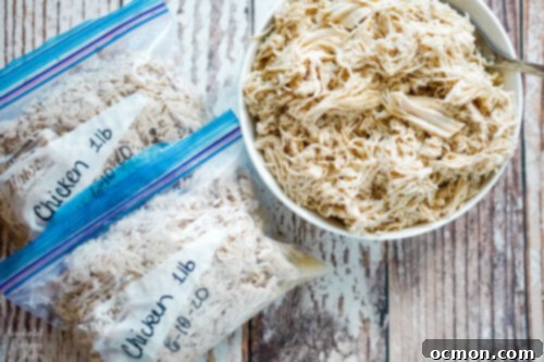 A white bowl full of shredded chicken with 2 freezer bags beside it. 