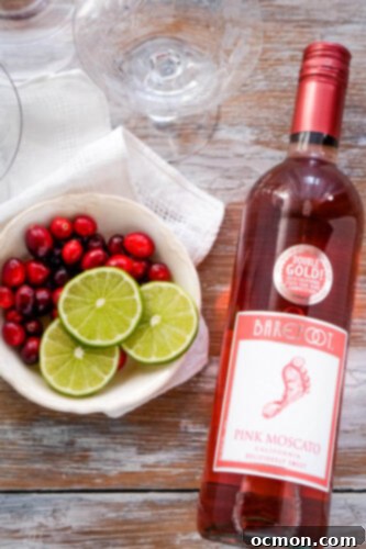 Sparkling Cranberry Moscato Punch 3 A bottle of pink moscato wine next to a bowl of fresh cranberries and sliced limes, ready for punch making.