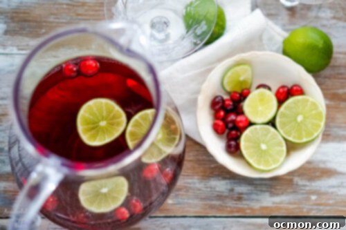 Sparkling Cranberry Moscato Punch 5 A pitcher of cranberry moscato punch with a bowl of sliced limes and cranberries next to it, ready for garnishing.