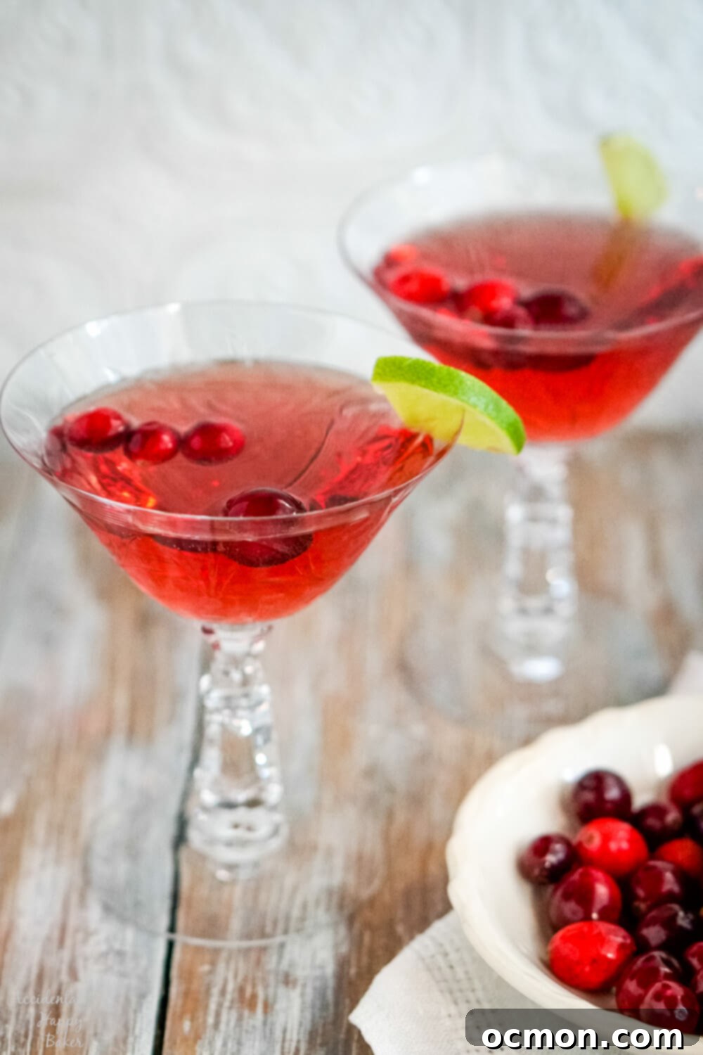Two crystal glasses of cranberry moscato punch, garnished with cranberries and lime.