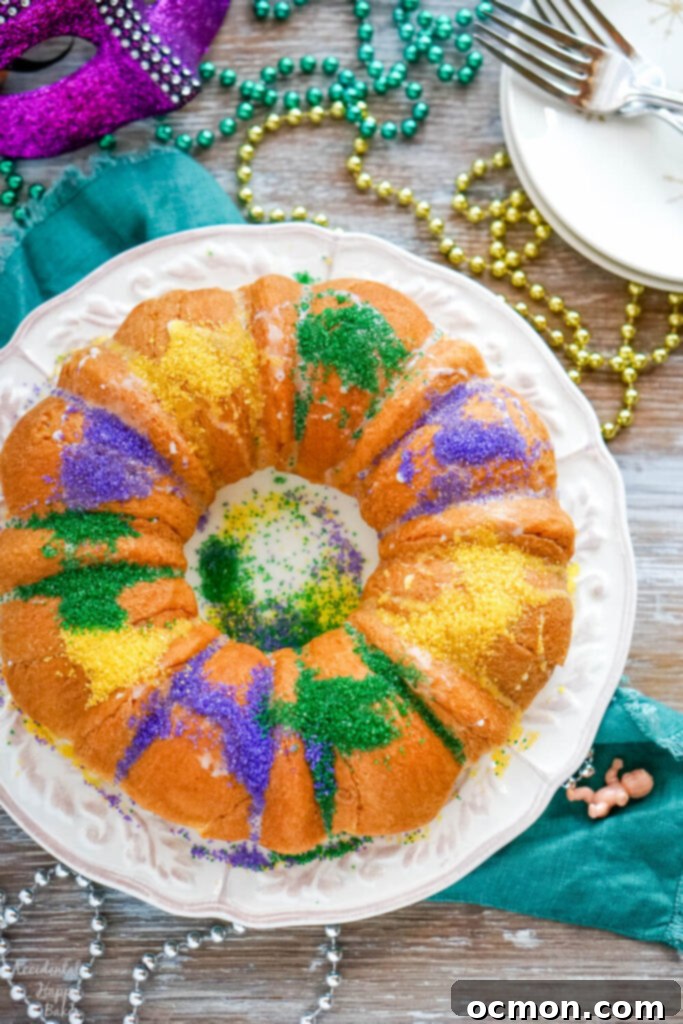 A white plate holding a king cake made from crescent rolls on a table spread with Mardi Gras beads.