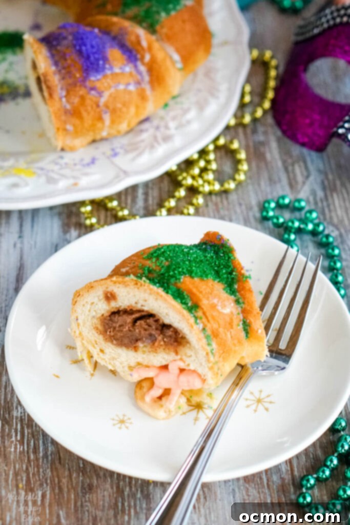 A slice of king cake on a white plate with mardi gras beads in the background. 
