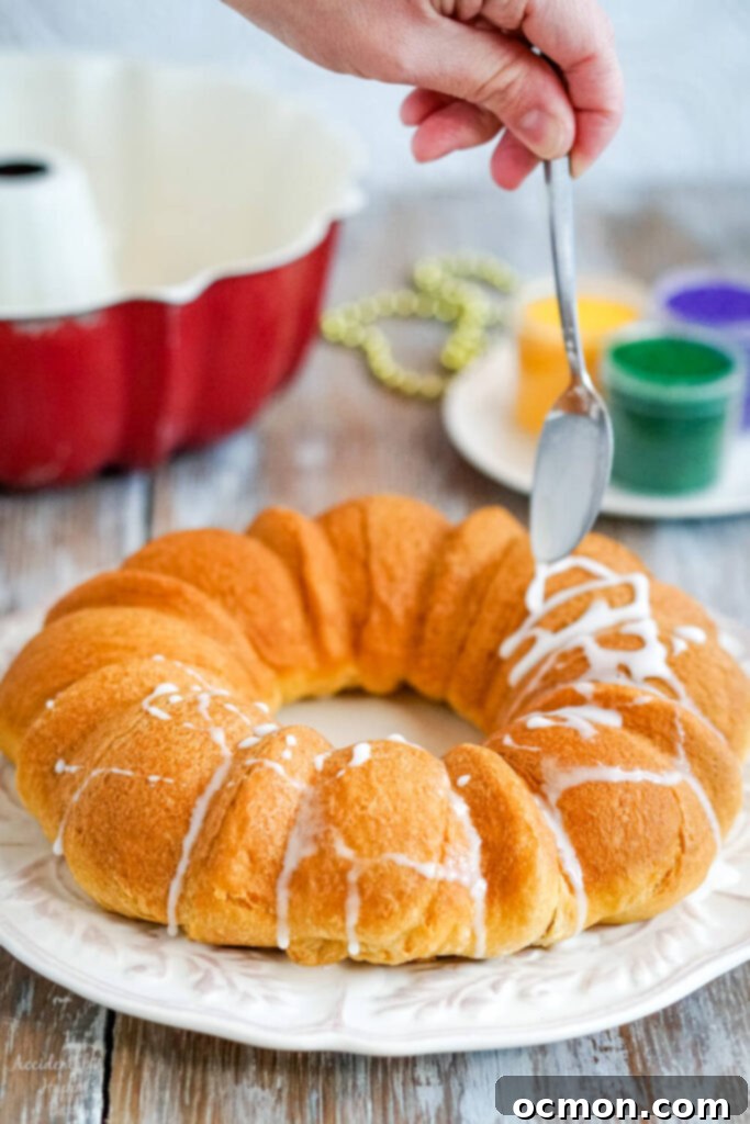 The baked king cake is drizzled with glazed before being decorated with colored sugar. 