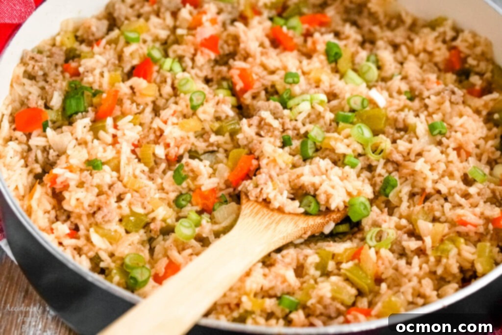 A skillet full of dirty rice with sausage with a wooden spoon holding a scoop of rice. 