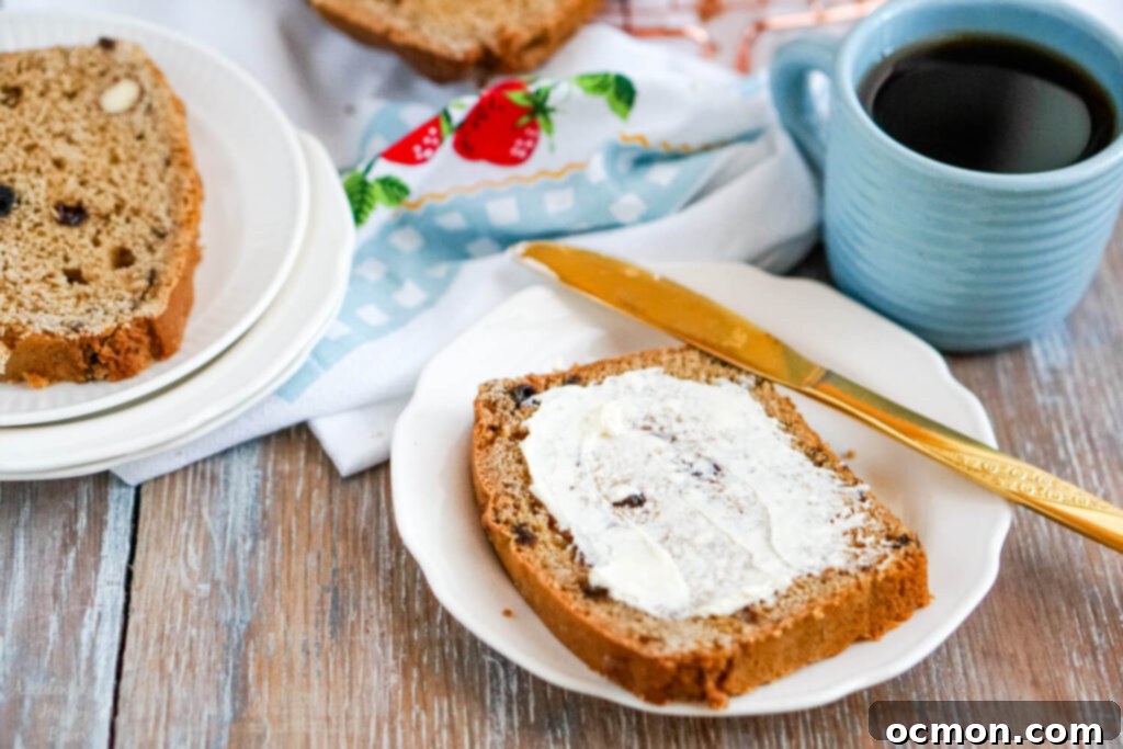 Welsh Bara Brith Tea Bread 3 A thick, inviting slice of Welsh tea loaf, generously slathered with rich butter, accompanied by a warm cup of tea.