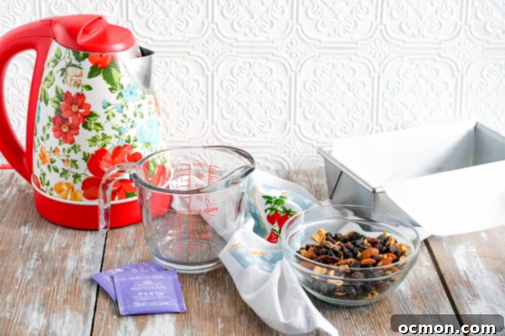 Welsh Bara Brith Tea Bread 5 A bowl filled with a colorful dried fruit blend positioned next to a clear measuring cup and an electric kettle, ready for steeping.