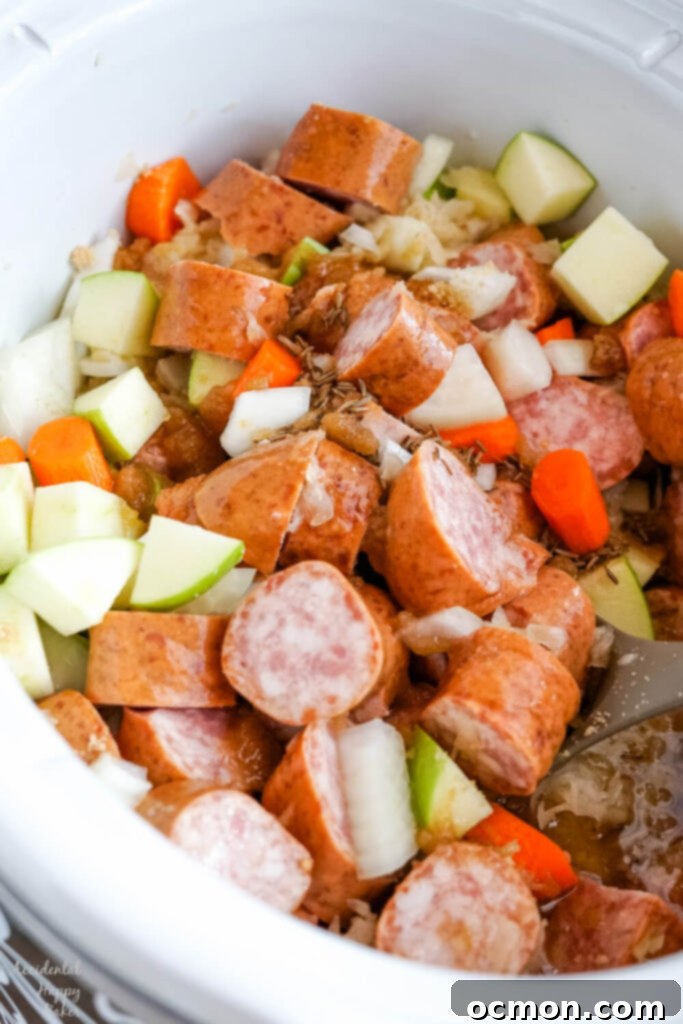 Brown sugar, caraway seeds, and apple juice are being poured over the kielbasa and vegetable mixture in the slow cooker.