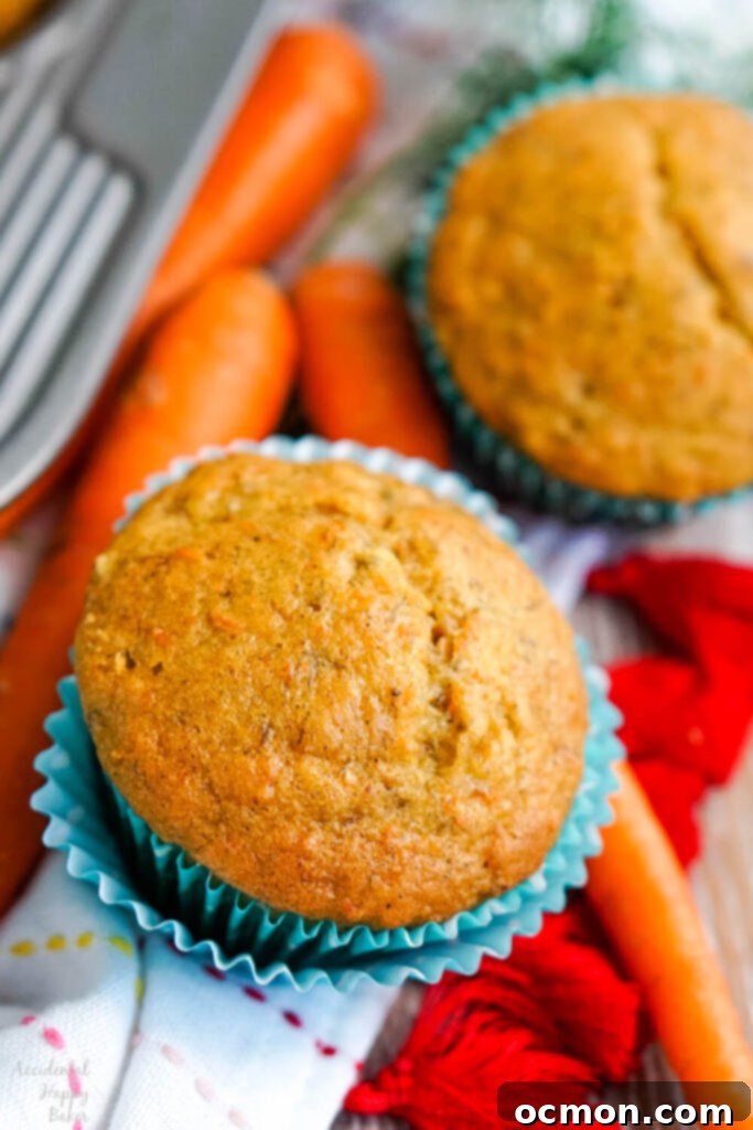 A single banana carrot muffin in a cupcake liner, with a fresh carrot beside it.