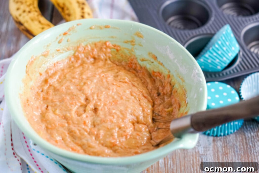 Muffin batter being scooped into a paper-lined muffin tin.