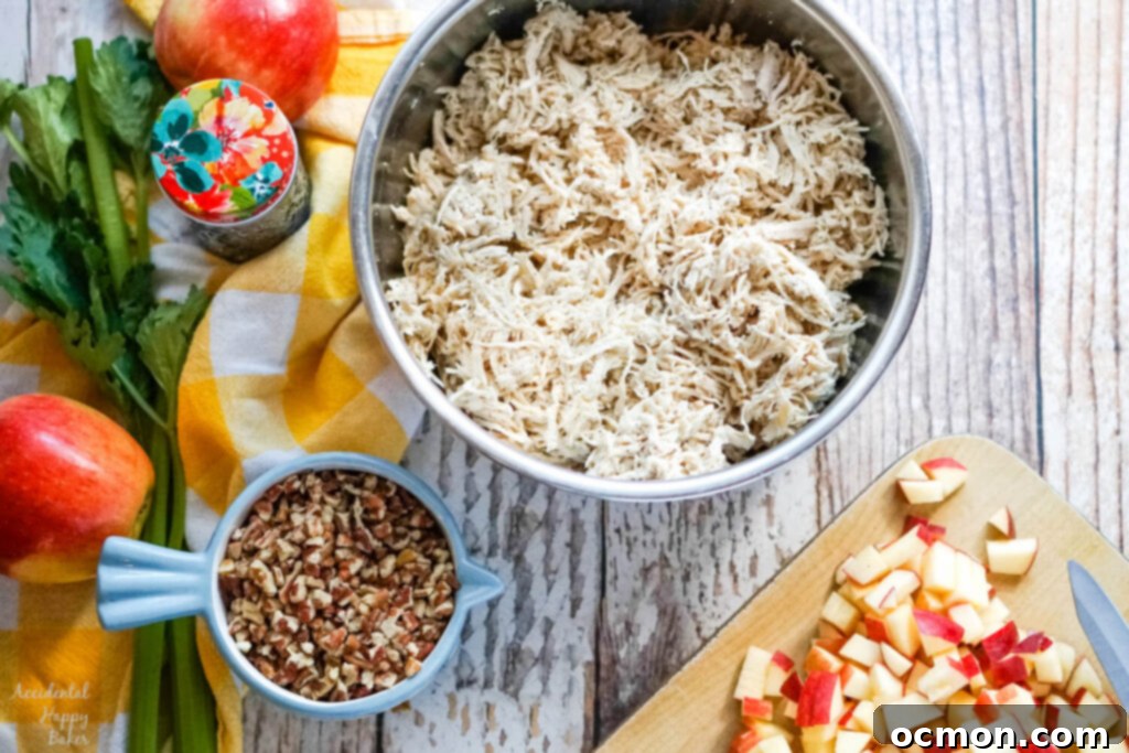Crisp Apple Pecan Chicken Salad 3 apples on a cutting board, chopped pecans in a measuring cup, and cooked and shredded chicken in a bowl