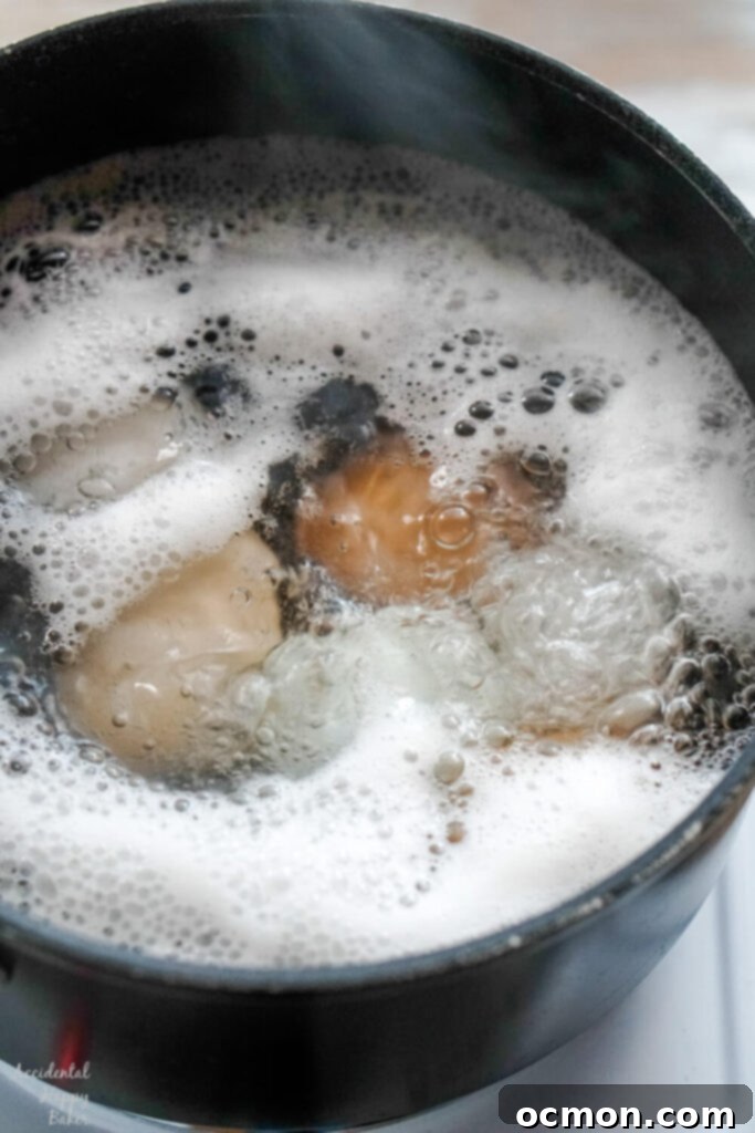 A saucepan filled with eggs in rapidly boiling water on a stovetop.