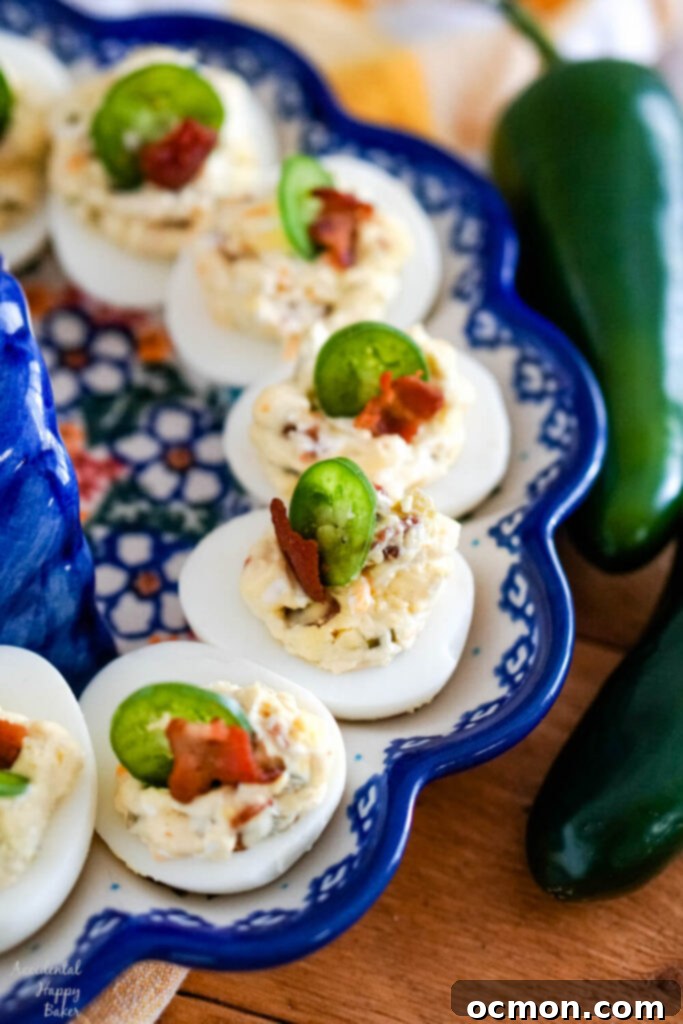 Devilish Jalapeno Poppers 2 A plate of jalapeno popper deviled eggs garnished with slices of jalapenos sitting next to jalapeno peppers.