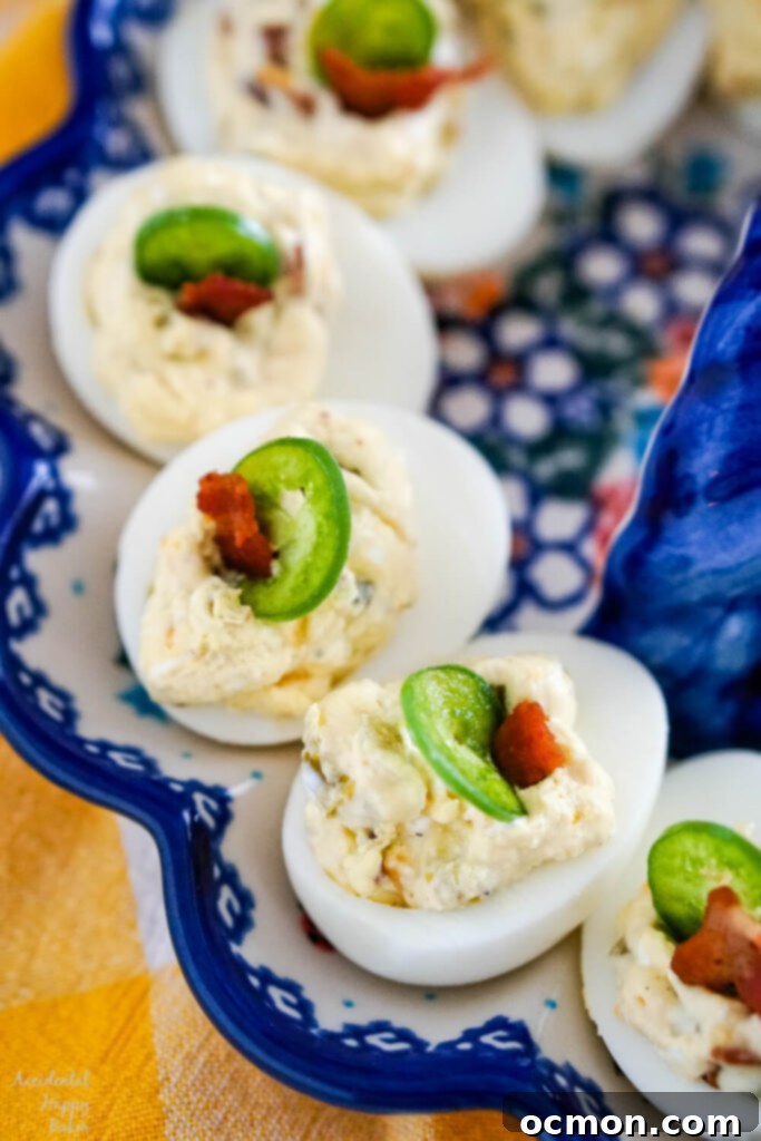 Devilish Jalapeno Poppers 9 Deviled eggs with a slice of jalapeno and a bit of bacon displayed on a egg plate.