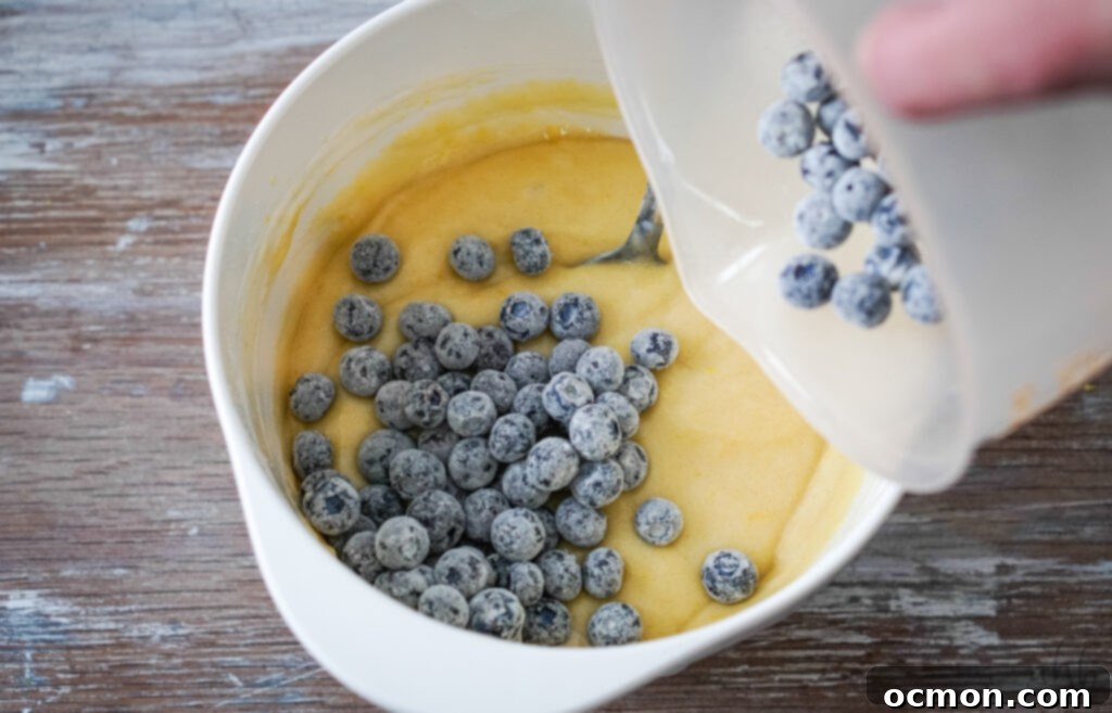 Zesty Lemon Blueberry Loaf with Creamy Buttermilk Glaze 4 Fresh blueberries are being gently coated with a light dusting of flour in a bowl before being folded into the quick bread batter.