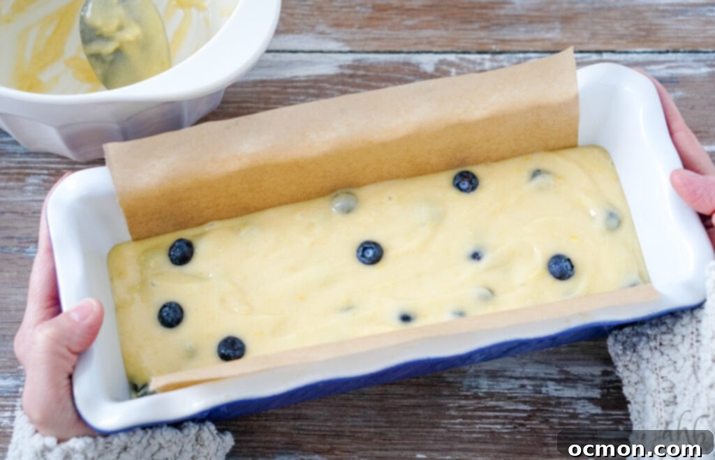 Zesty Lemon Blueberry Loaf with Creamy Buttermilk Glaze 5 A loaf pan meticulously lined with parchment paper, filled with the rich lemon blueberry bread batter, perfectly prepped and ready for baking in the oven.