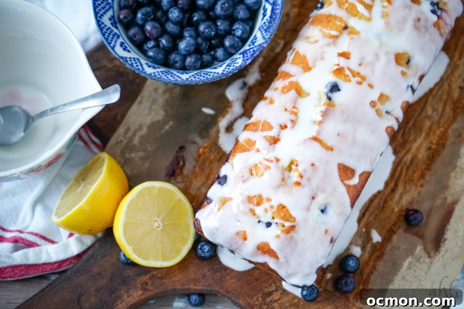 Zesty Lemon Blueberry Loaf with Creamy Buttermilk Glaze 7 A beautiful loaf of lemon blueberry bread with a delicate buttermilk glaze, presented on a rustic bread board with fresh lemons and blueberries arranged artfully to one side, capturing its fresh appeal.