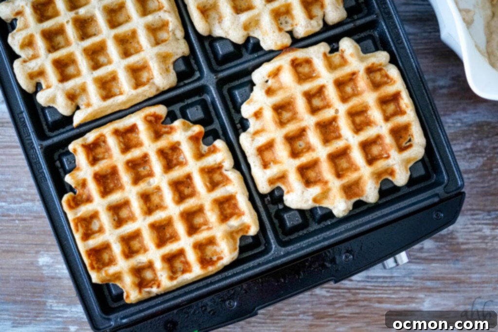 Freshly cooked oatmeal waffles being removed from a waffle maker.