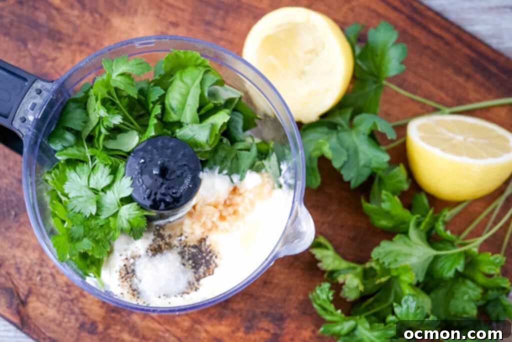 A food processor containing the fresh ingredients for the creamy herbed lemon dressing with mayo, ready to be blended.