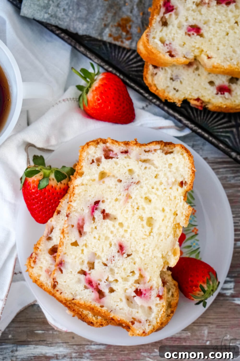 Two generous slices of homemade Strawberry Yogurt Bread displayed on a white plate, garnished with fresh strawberries, showcasing its inviting appearance.