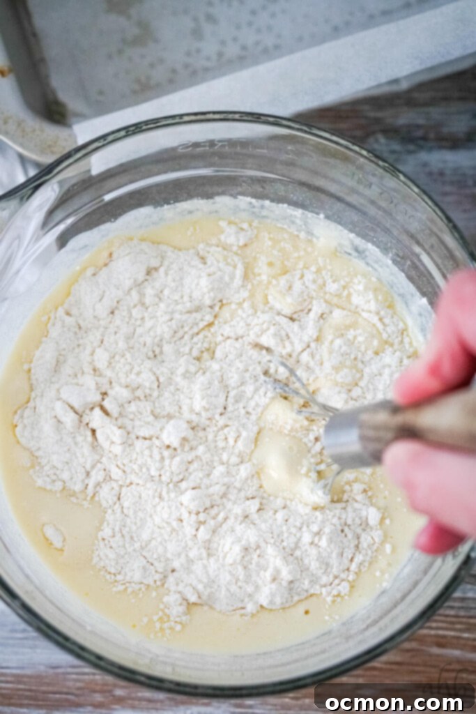 The wet ingredients are poured into the bowl of dry ingredients, ready to be gently mixed until just combined, preventing overmixing.