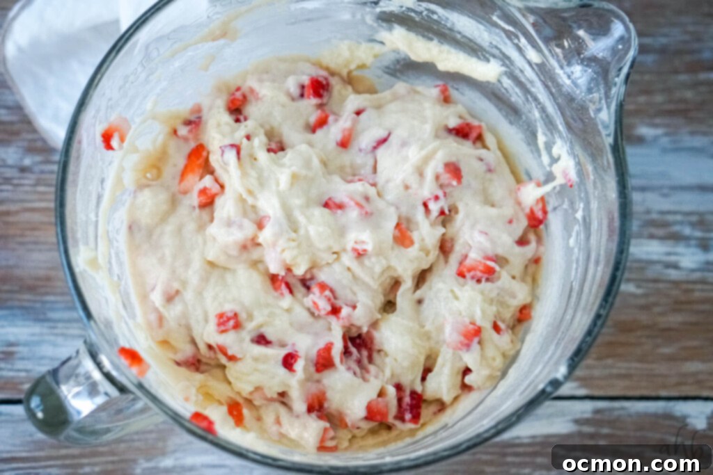 Finely diced strawberries are gently tossed into the bread batter and folded in, ensuring they are evenly distributed without bruising.