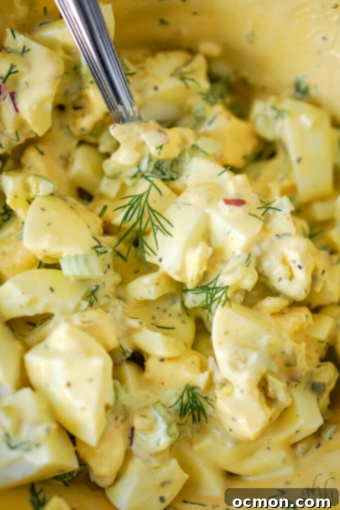 Grandma's Classic Egg Salad 6 A close-up shot of a bowl of creamy, yellow homestyle egg salad, garnished with fresh green dill, highlighting its appealing texture and color.