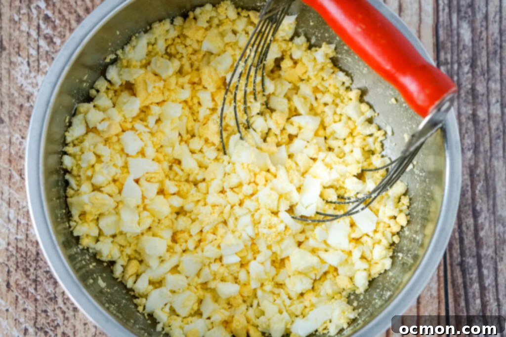 Grandma's Classic Egg Salad 7 A white bowl filled with roughly chopped hard-boiled eggs, with a stainless steel pastry blender resting beside it, ready for use.