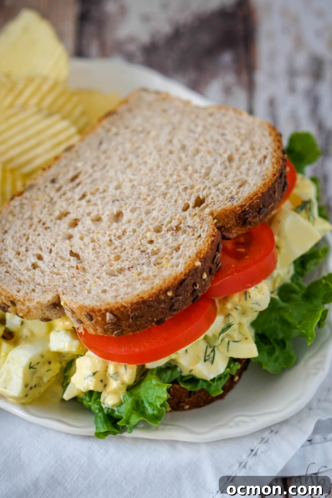 Grandma's Classic Egg Salad 8 A homestyle egg salad sandwich with lettuce and tomato on a white plate.