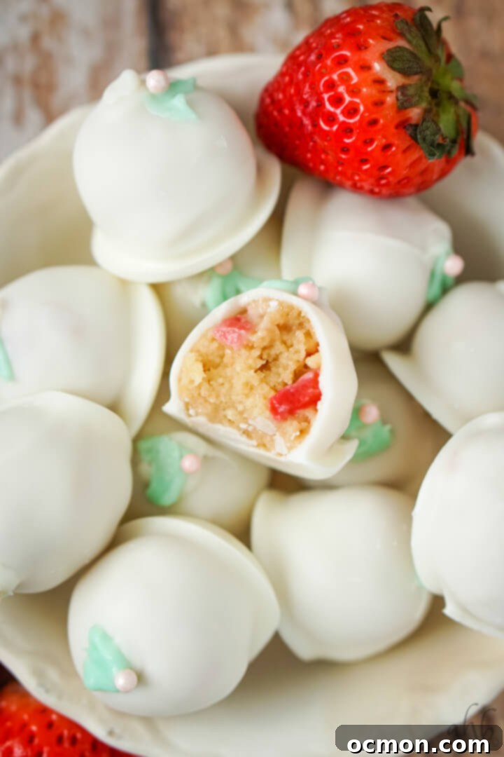 A bowl full of strawberry cheesecake truffles with 2 fresh strawberries to the side.