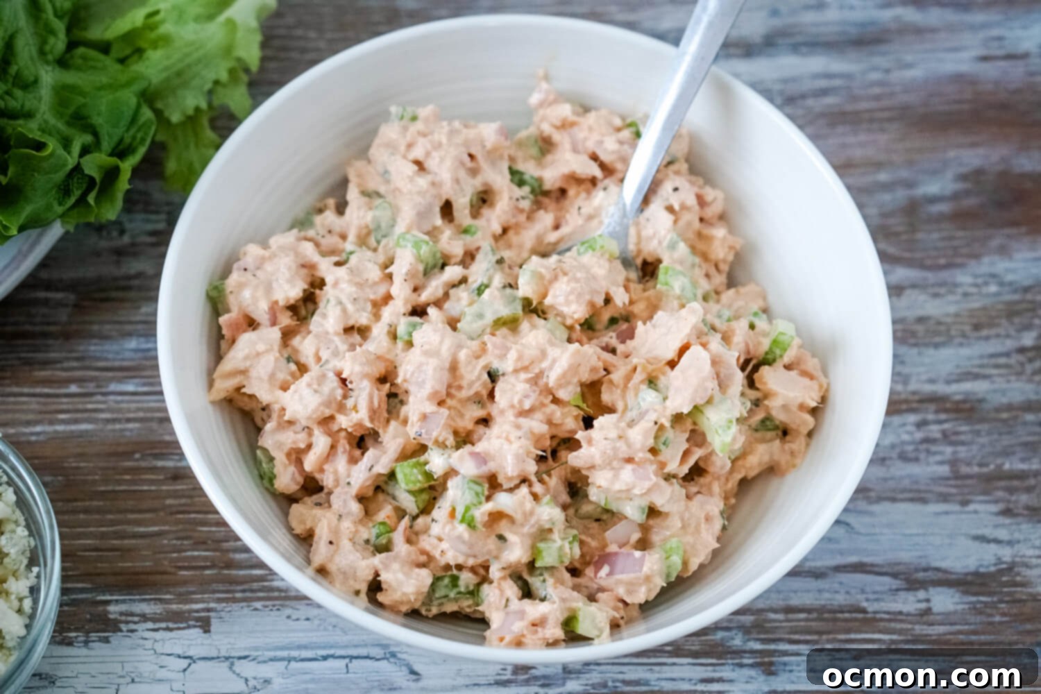 A white bowl full of buffalo tuna salad with a plate of lettuce leaves to one side.