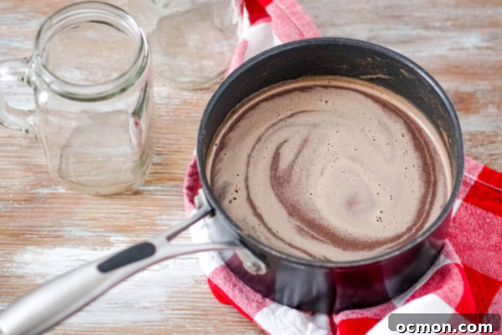 Decadent Peanut Butter Hot Chocolate 5 A saucepan on the stove filled with peanut butter hot chocolate being whisked, showing the melting ingredients.
