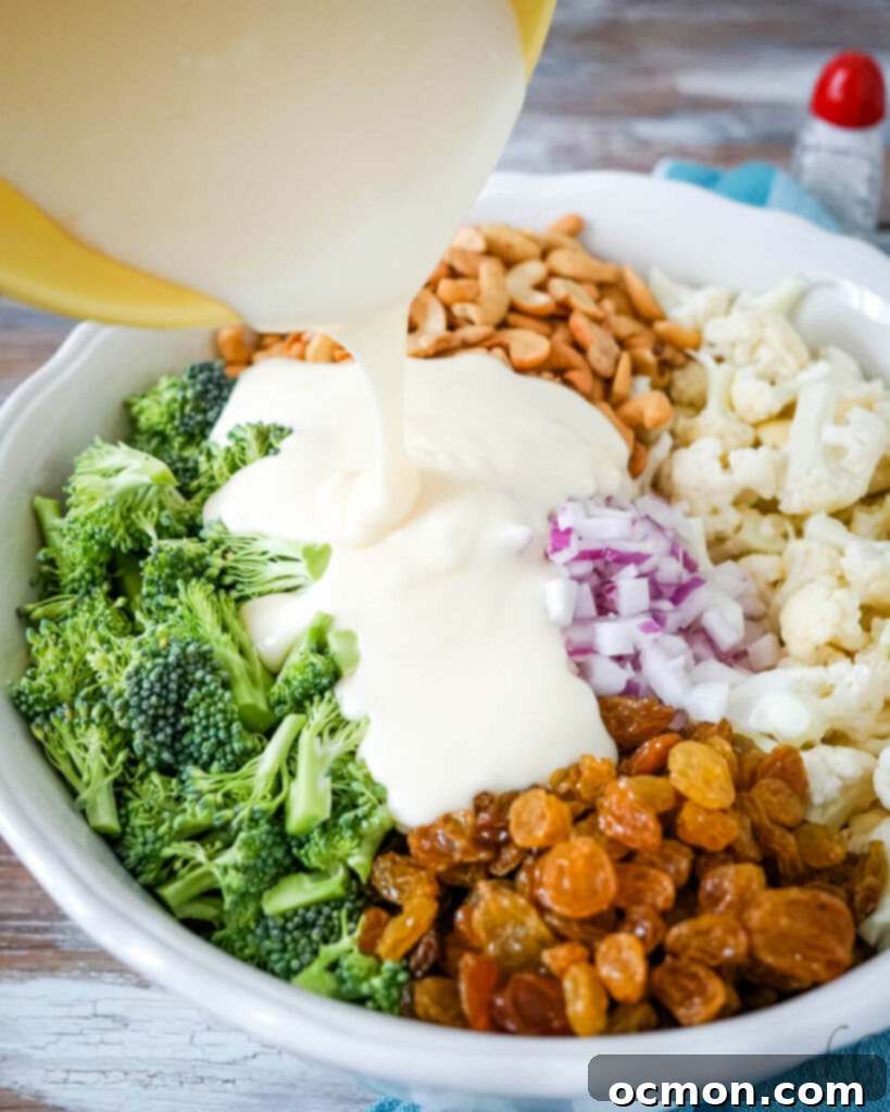 Amish-Style Creamy Broccoli and Cauliflower Salad 6 The rich, creamy dressing is poured over the colorful mix of vegetables, nuts, and raisins in a large bowl, ready to be combined.
