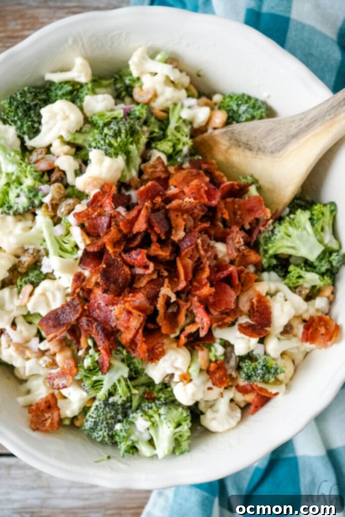 Amish-Style Creamy Broccoli and Cauliflower Salad 7 Crispy crumbled bacon being carefully stirred into the prepared Amish Broccoli Cauliflower Salad, just before it's served.