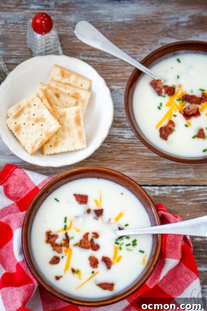 Two steaming bowls of 4-ingredient potato soup served alongside a white bowl brimming with crispy saltine crackers, ready for a comforting meal.