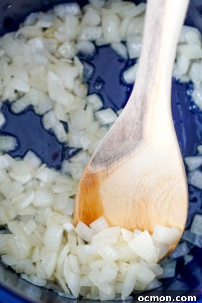 Finely diced yellow onion sautéing in rendered bacon grease, stirred gently with a wooden spoon in a large blue stockpot, creating an aromatic base for the soup.