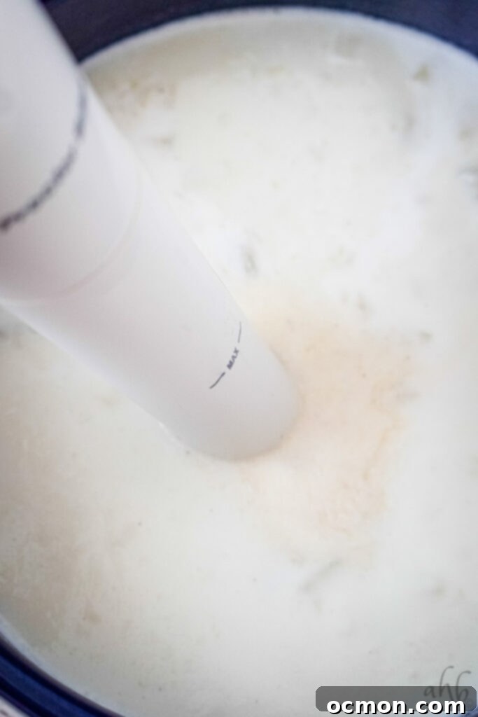 An immersion blender is actively blending the cooked potatoes and half and half directly in the stockpot, transforming the mixture into a thick and creamy 4-ingredient potato soup.