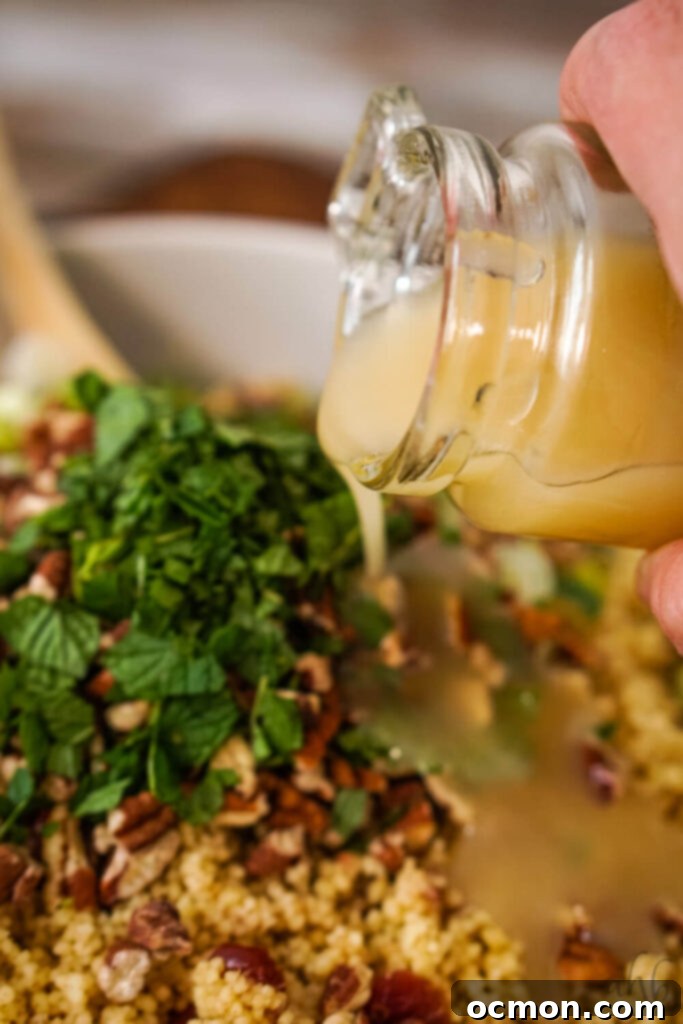 The homemade sweet and tangy dressing being drizzled generously over the top of the vibrant Cranberry Couscous Salad in a white bowl, ready to be tossed and served.