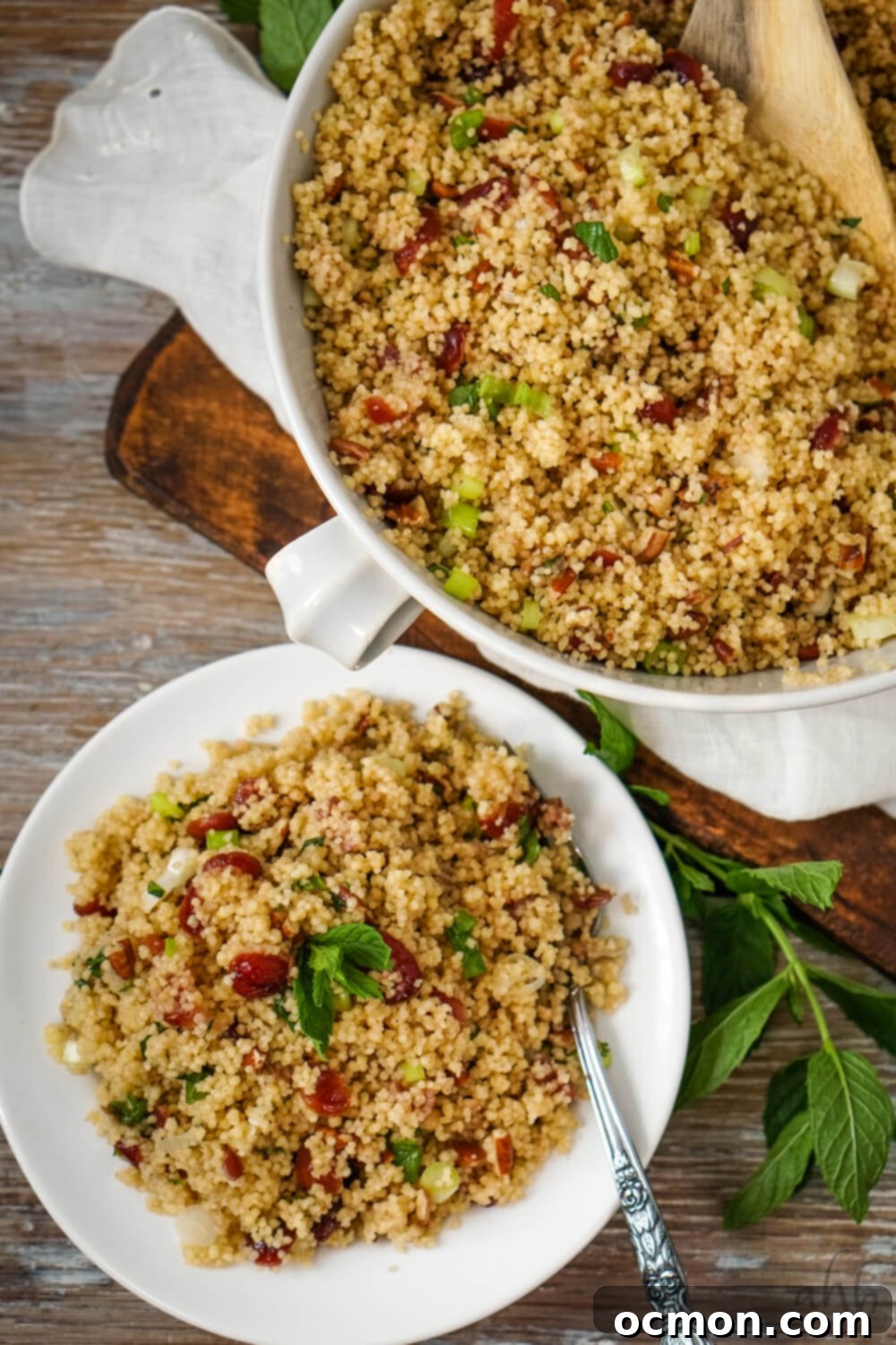 A vibrant individual serving of Cranberry Couscous Salad on a white plate next to a larger white serving bowl brimming with more salad, elegantly presented and ready for sharing at a meal.